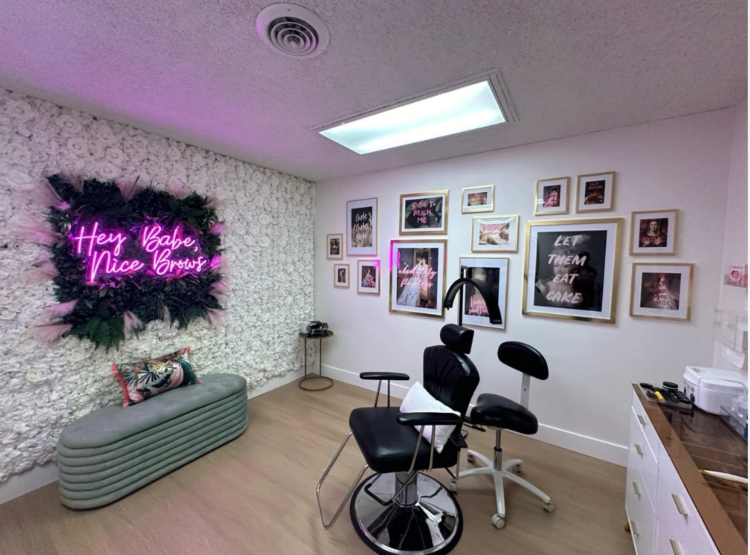 Inside Browza Studio: a white flower wall with a pink neon sign reading Hey Babe, Nice Brows, a gallery wall, and the brow chair